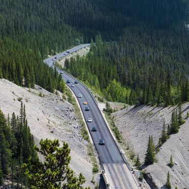 A winding road through a mountainous forest with several cars driving.