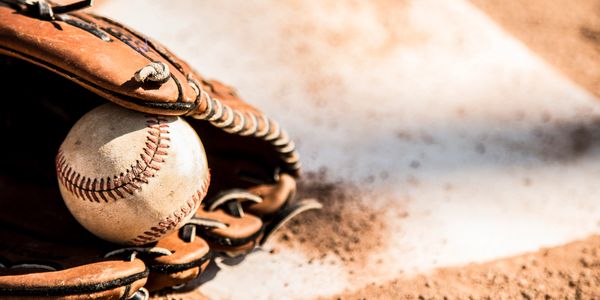 A worn baseball resting in a leather glove on a dirt field.