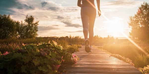 Person jogging on a wooden path during sunset.