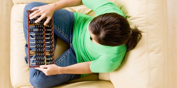 Young woman using an abacus while sitting on a beige couch.