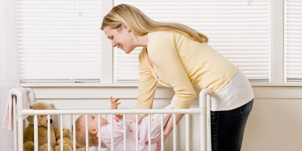A mother joyfully interacts with her baby in a white crib.