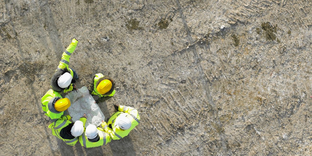 Construction workers in safety gear examining a site plan on a rough terrain.