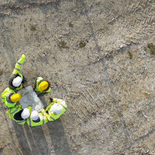 Construction workers in safety gear reviewing plans on a dirt site.