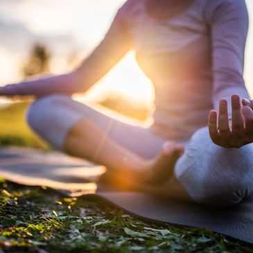 Person meditating outdoors on a yoga mat during sunset.