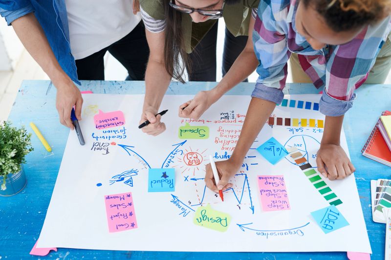 Top view at multi-ethnic group of  young people drawing charts and graphs while planning startup project standing at desk and communicating actively
