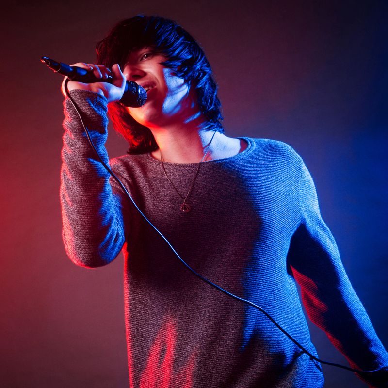 The young male vocalist or singer is singing with microfon on the stage on concert with colorful concert lights.