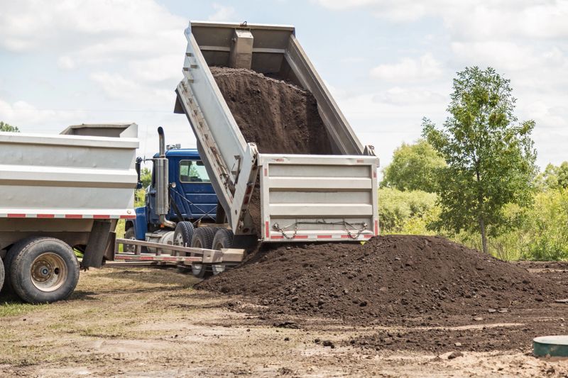 A truck is dumping a load of black dirt for use in the installation of a new mound septic system.