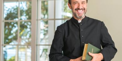 Smiling priest holding a Bible indoors.