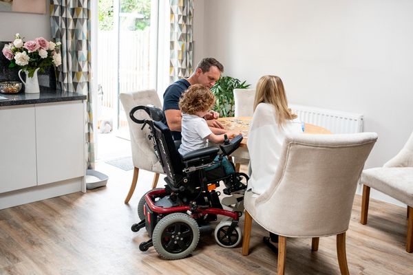 Family playing puzzle at dining table; child in wheelchair included.