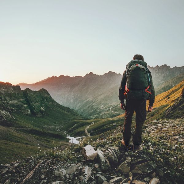 A hiker with a backpack overlooking a scenic mountain valley at sunrise.