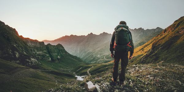 A hiker with a backpack overlooking a scenic mountain valley at sunrise.