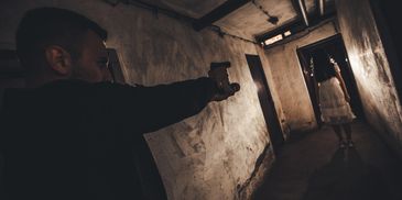 A man points a gun at a woman standing in a dimly lit hallway.