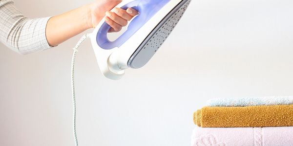 Person ironing clothes with a modern steam iron near folded towels.