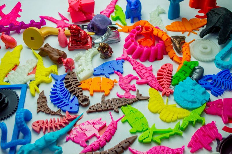 Many bright multi-colored objects printed on 3d printer lie on flat surface close-up. Fused deposition modeling, FDM. Concept modern progressive additive technology for 3d printing.