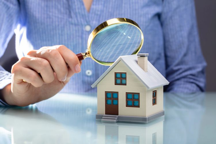 Person inspecting a miniature house with a magnifying glass.