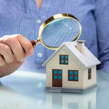 Person inspecting a miniature house with a magnifying glass.