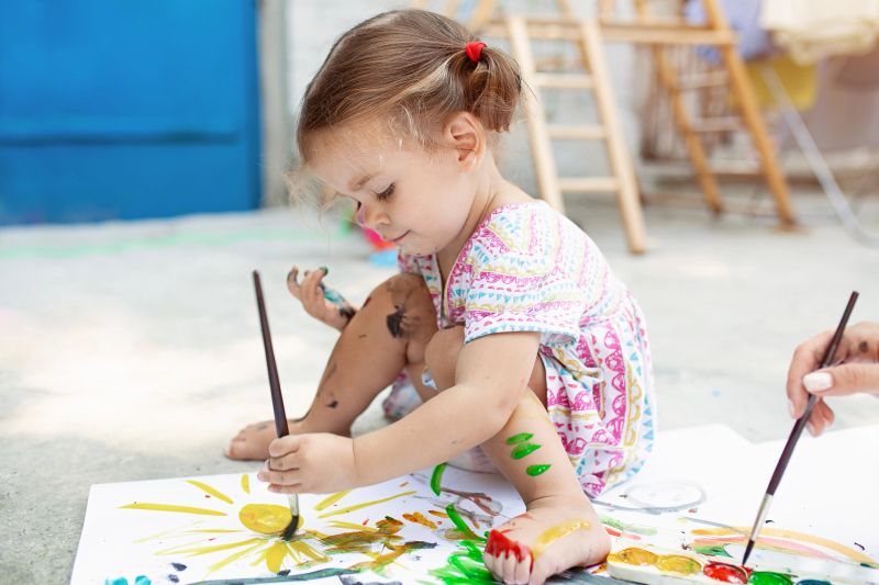 Cute little caucasian Girl enjoying Painting at the backyard with paper, water colour and art brush. Selective focus.