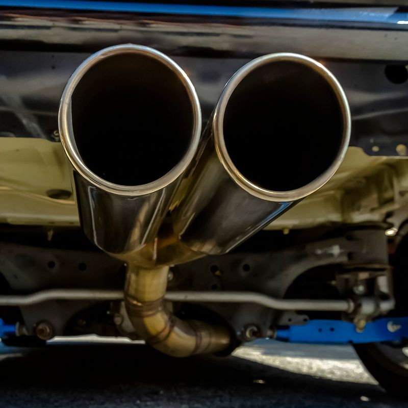 Close up of dual exhaust pipe at the back of car. Close up view of binary chrome muffler attached to the back of a car. A partial view of the tires and under chasis can also be seen.