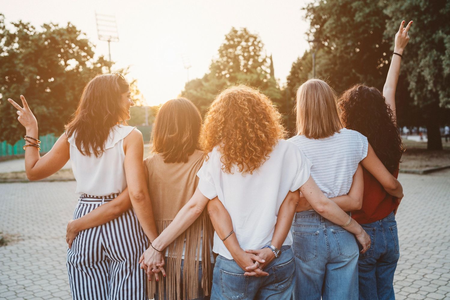 Five women standing arm in arm, enjoying a sunset outdoors.