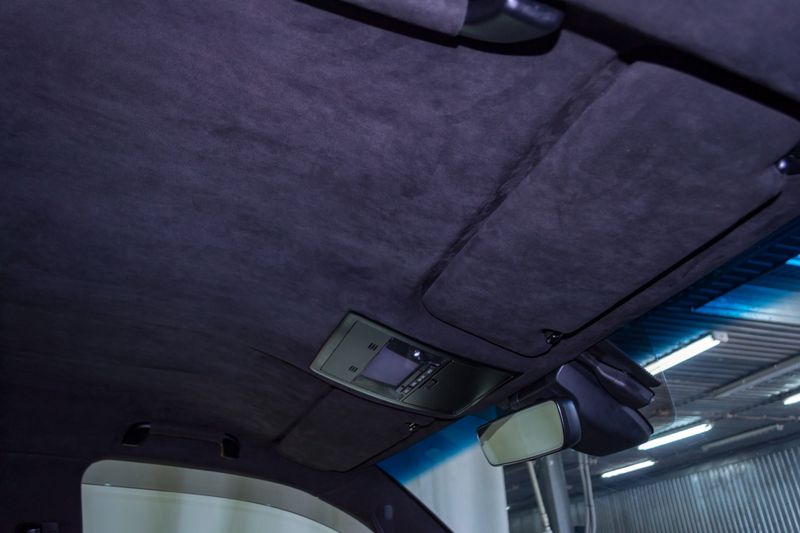 The ceiling of the SUV car pulled by black soft material alkantara in the workshop for tuning and styling the interior, view from the passanger opened door on central mirror and sun visorson the roof