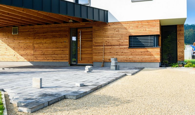 Laying gray concrete paving slabs in house courtyard driveway patio. Professional workers bricklayers are installing new tiles or slabs for driveway, sidewalk or patio on leveled foundation base made of sand at public or private residence.