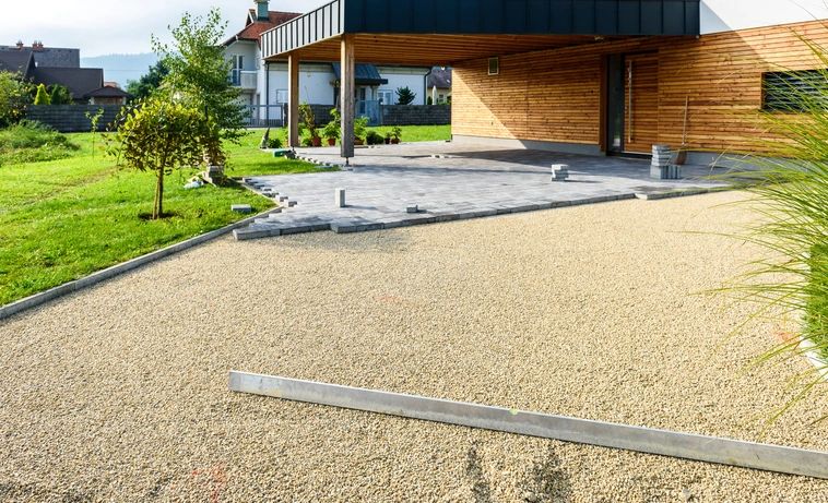 Laying gray concrete paving slabs in house courtyard driveway patio. Professional workers bricklayers are installing new tiles or slabs for driveway, sidewalk or patio on leveled foundation base made of sand at public or private residence.