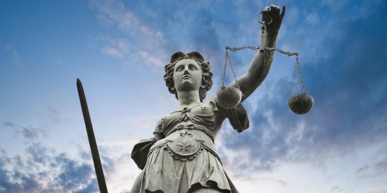 Statue of Lady Justice holding scales and sword against a blue sky.