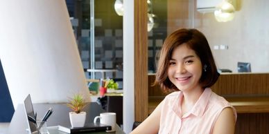Young woman smiling at desk with laptop and calculator in modern office.
