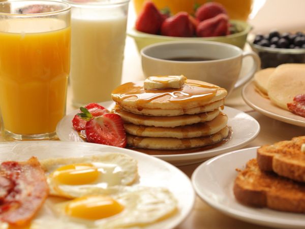 A classic breakfast with pancakes, eggs, bacon, toast, and drinks.