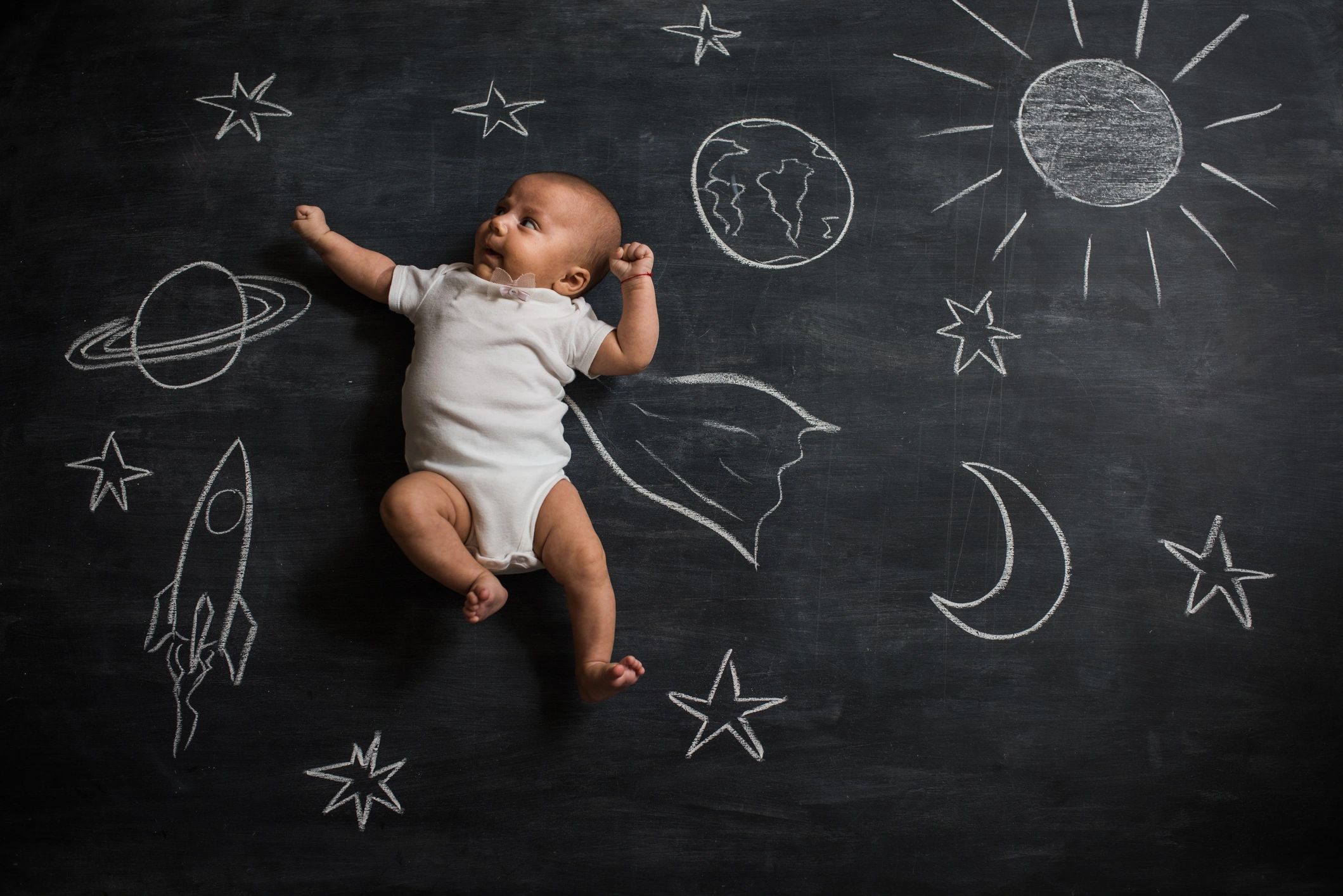 Baby lies on a chalkboard with space-themed drawings around.