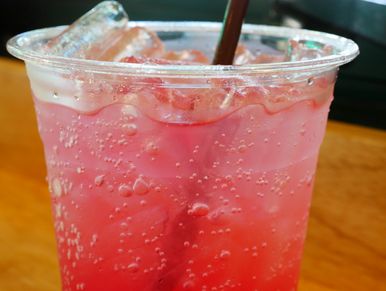 A pink fizzy drink with ice in a plastic cup.