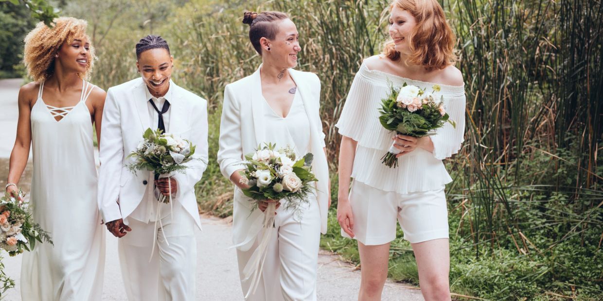 Four people in white outfits holding bouquets, walking outdoors.