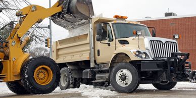 Loader dumping snow into a dump truck.