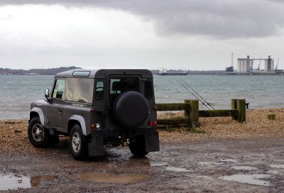 Black SUV parked near a beach on a cloudy day.