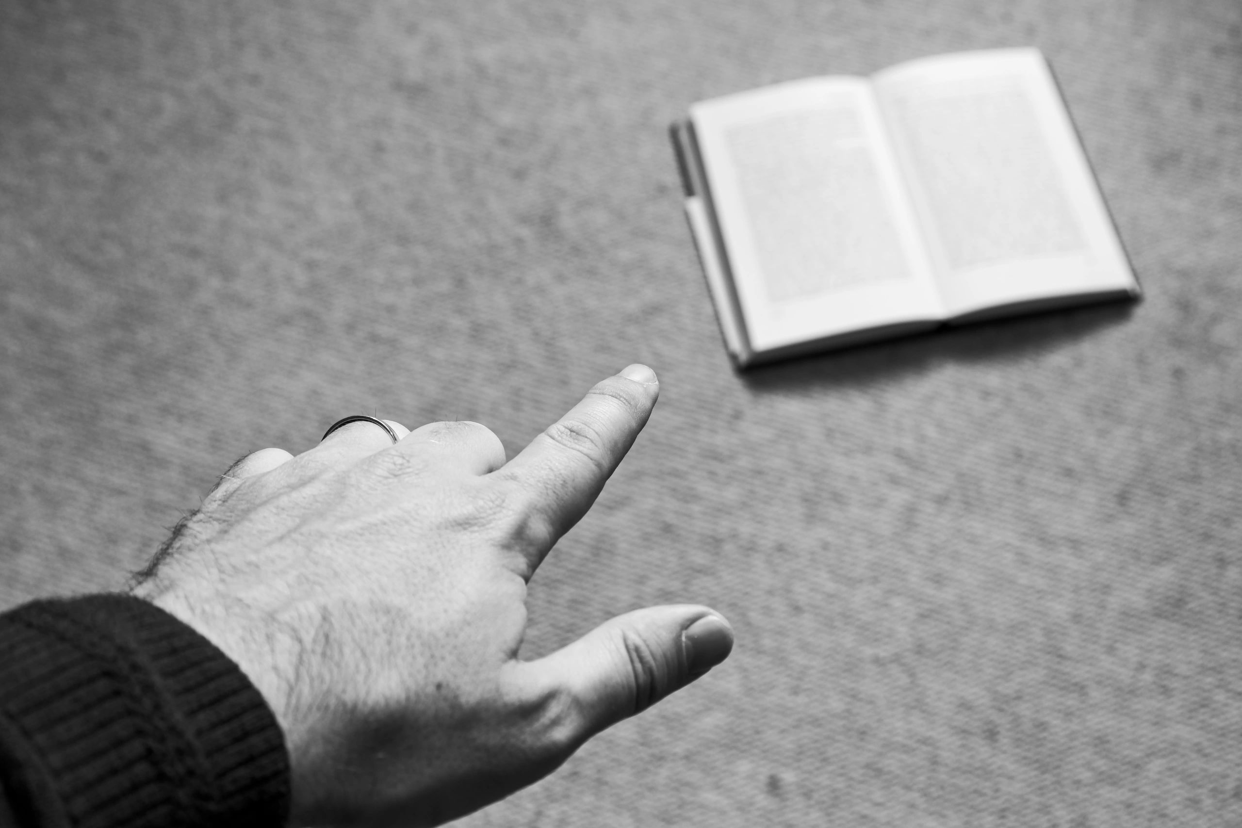 A hand pointing at a book. This image can be used to represent the concept of being instructed to study by somebody.