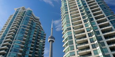 Two modern high-rise buildings with the CN Tower in between against a clear blue sky.