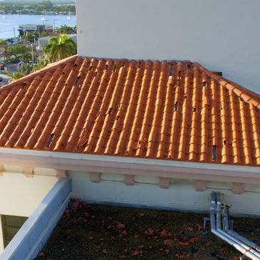 Damaged terracotta tile roof with broken and missing tiles on a building.