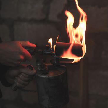 Hands holding a vintage blowtorch with bright flames.