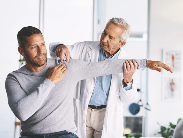 Doctor assisting a man with shoulder movement exercises.