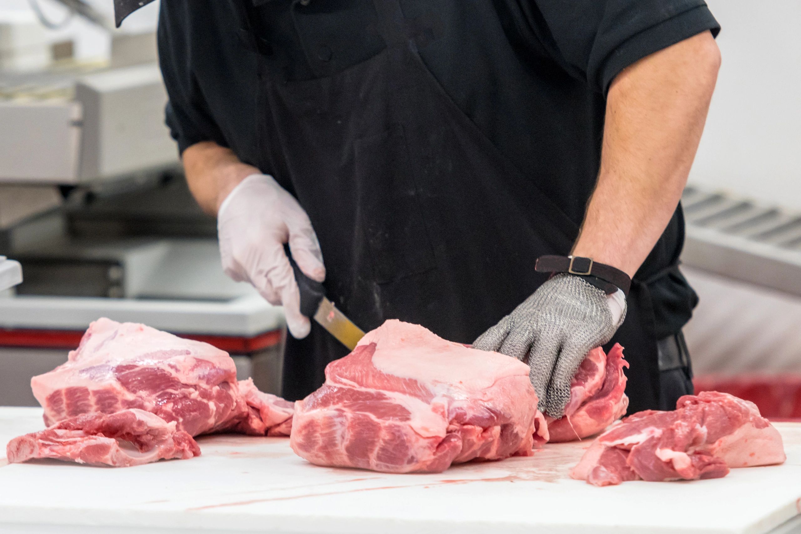 Butcher cutting fresh pork meat with safety gloves.