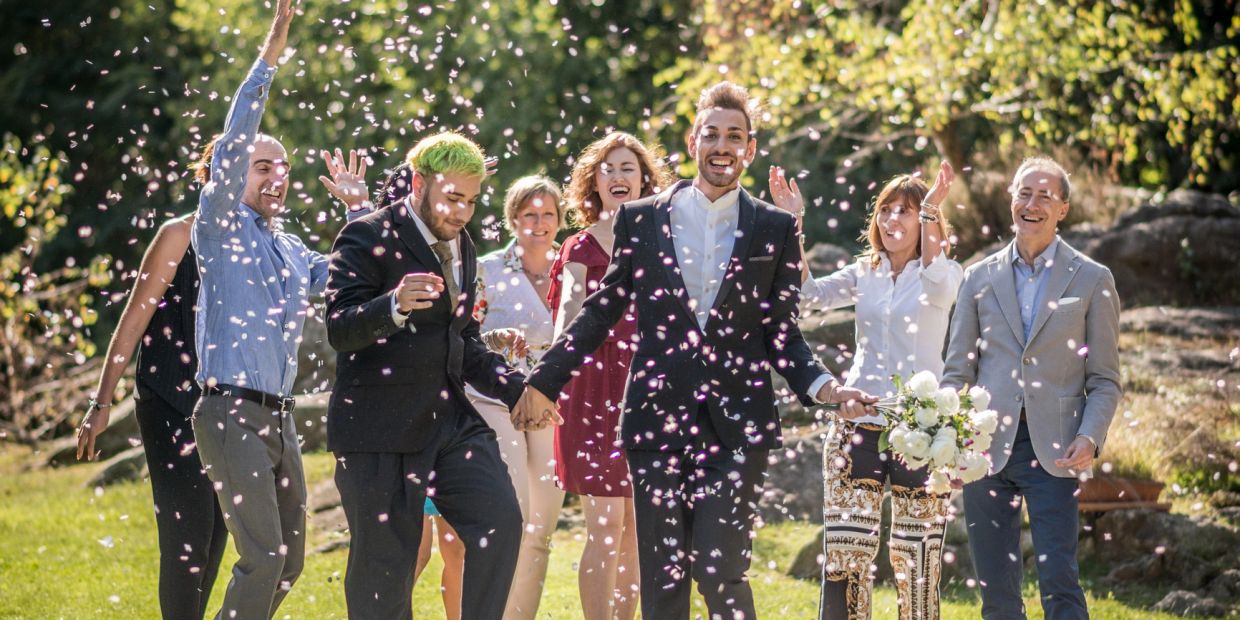 Two grooms and their friends celebrate outdoors with confetti and smiles.