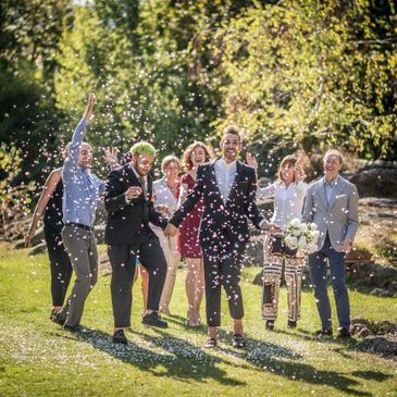Joyful wedding celebration with friends throwing confetti outdoors.