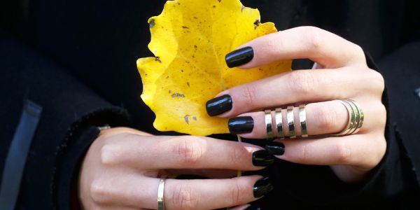 Hands with black nail polish holding a yellow leaf.