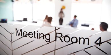 People in a blurred office meeting behind an etched glass door labeled Meeting Room 4.