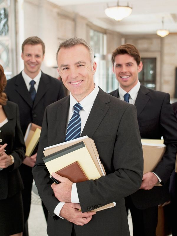 A group of five business professionals holding files and smiling.