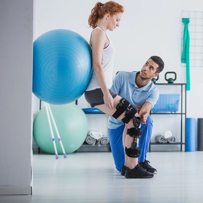 Physical therapist assisting woman with knee brace during exercise using a stability ball.