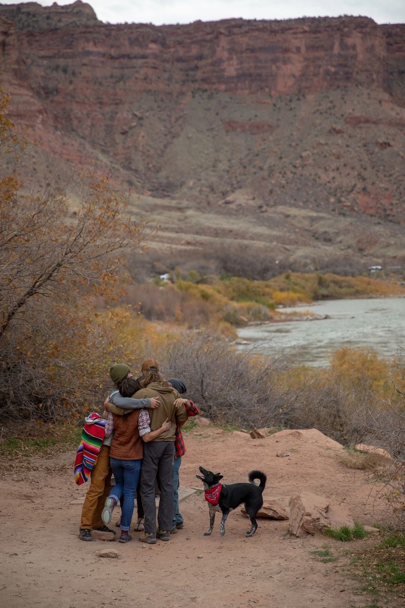 Dog watches while group of excited friends hug at an empty lakeside campsite in Moah, Utah.