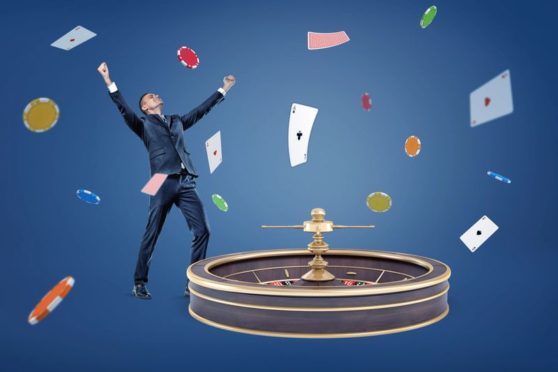 A happy businessman stands with raised hands near a large roulette and under a rain of cards and chips. Casino and lottery. Big money win. Prize money.