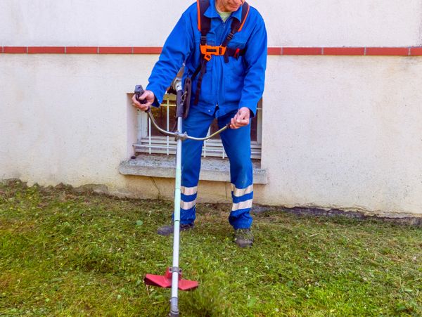 Worker in blue uniform trimming grass with a string trimmer.
