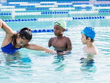 A swim instructor teaches two children in a pool.